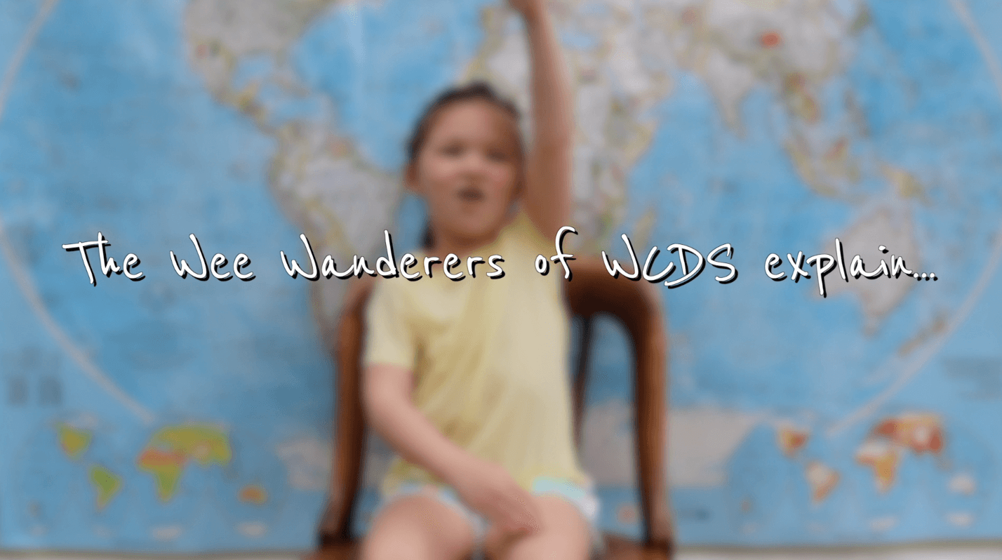 The Wee Wonders of WCDS Explain with a child in front of a map with her hand raised high in the air.